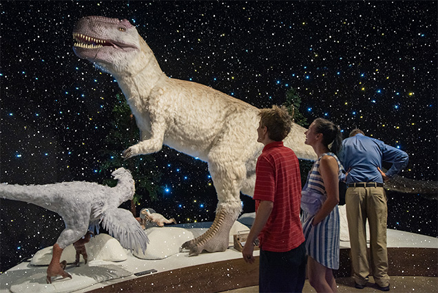 Three people looking at animatronic dinosaurs.